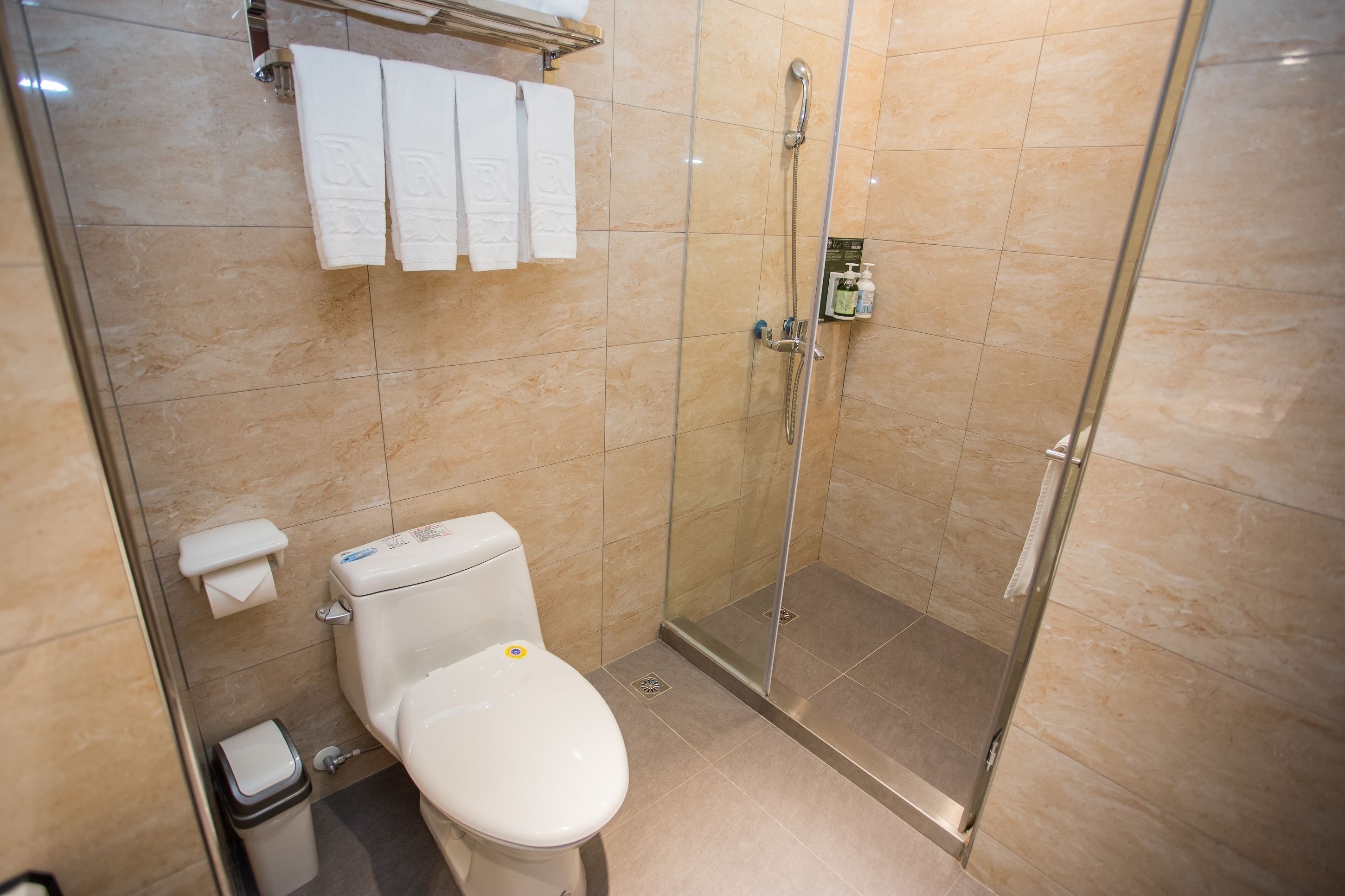 Un baño con inodoro, cabina de ducha de vidrio y un perchero con tres toallas.