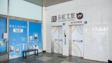 A hotel entrance with a blue wall featuring a FamilyMart collection advertisement, a bench, and two elevator doors with colorful designs.
