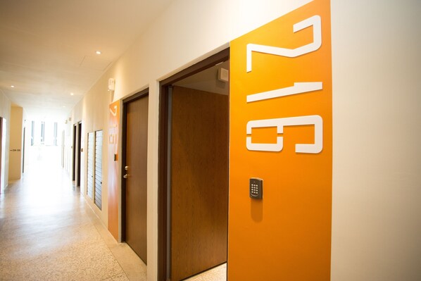 Un couloir d’hôtel avec des portes numérotées, dont la porte 216, un couloir avec un revêtement de sol de couleur claire, et une porte dotée d’un système de verrouillage à clavier.