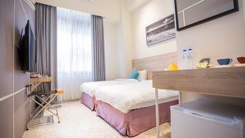 A hotel room with two beds, a TV, a mini-fridge, a desk, and a window with curtains.