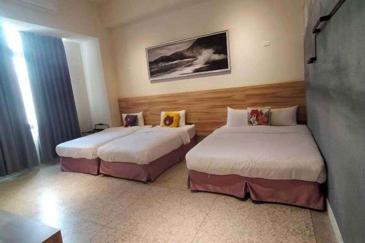 A hotel room with two beds, a wooden headboard, a painting on the wall, and a window with curtains.