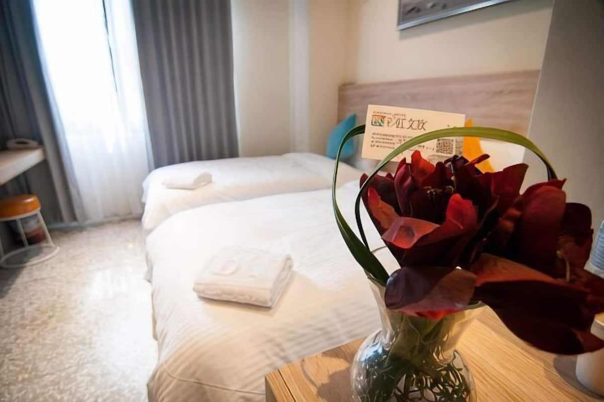 Una habitación de hotel con dos camas, un jarrón con flores y un cartel con texto.