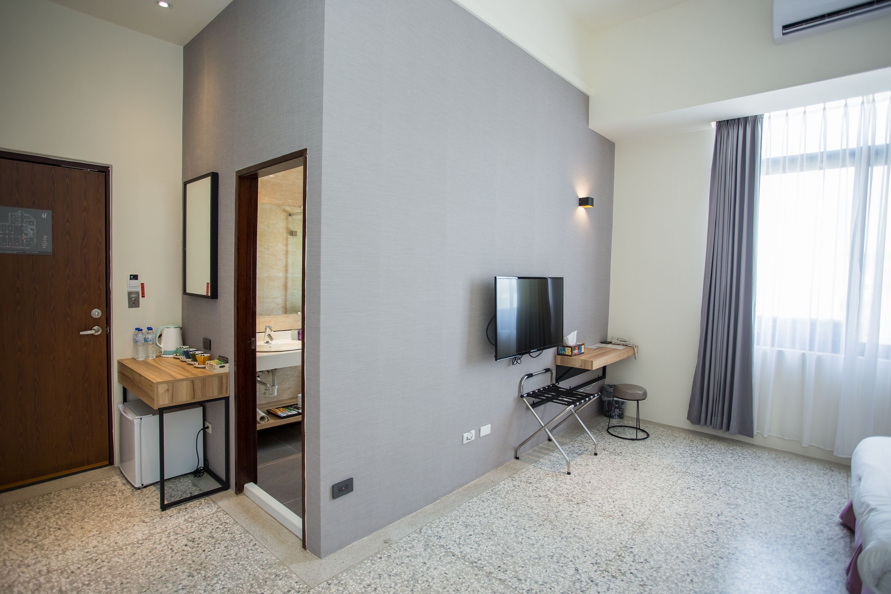 Une chambre d’hôtel moderne dotée d’une kitchenette, d’un téléviseur à écran plat, d’un petit coin salon et d’une grande fenêtre avec des rideaux.