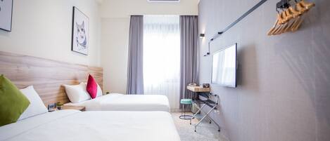 A hotel room with two beds, a desk, a chair, an air conditioning unit, a TV, and a window with curtains.