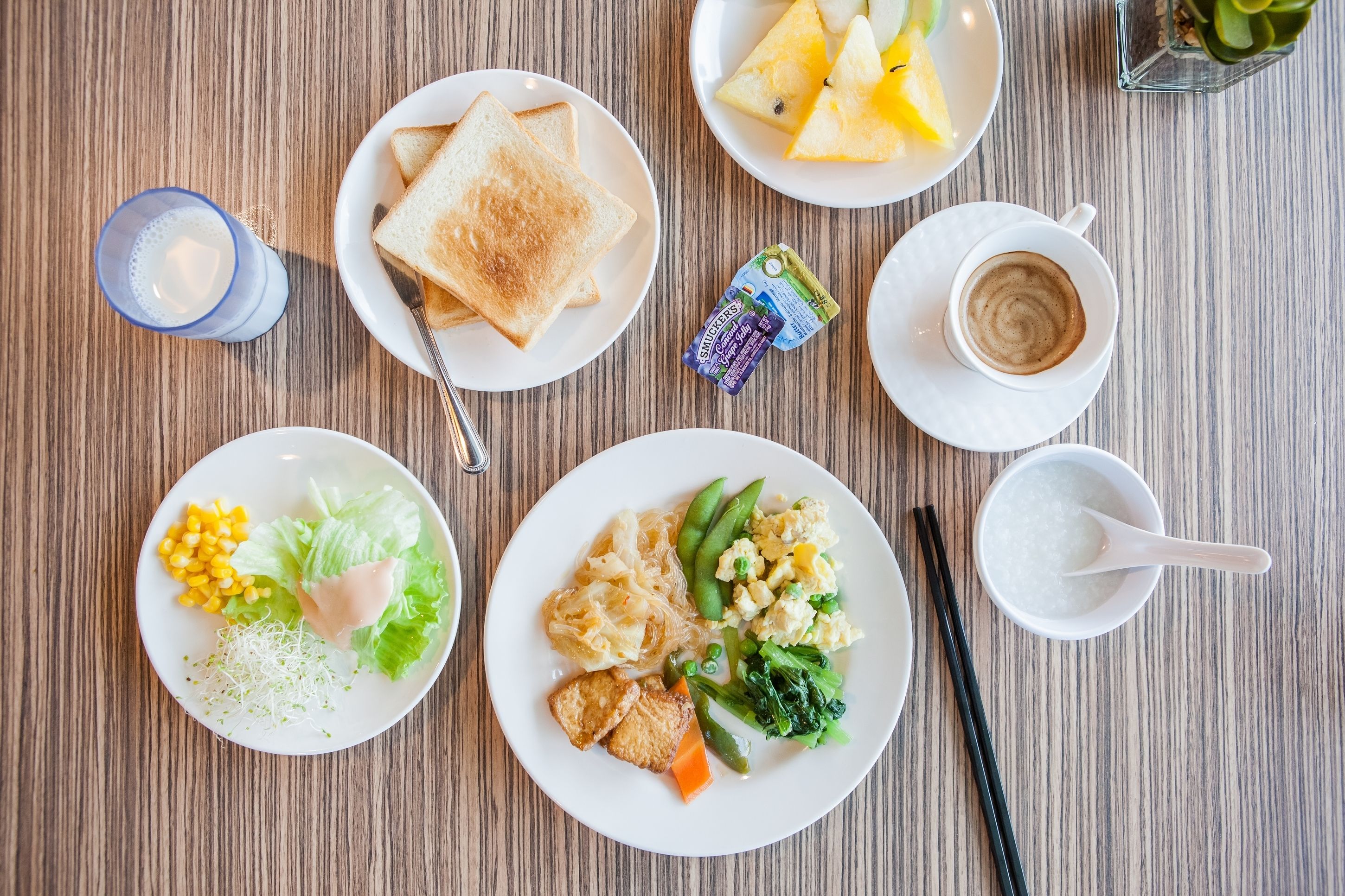 A wooden table with various food items including plates of toast, fruit, and a cup of coffee.