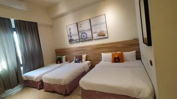 Quarto de hotel com duas camas de solteiro e uma cama maior, cabeceira de madeira e três quadros na parede.