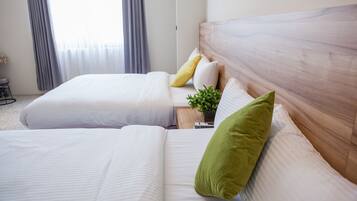 Quarto de hotel com duas camas, cabeceira de madeira, uma mesinha com uma planta e uma janela com cortinas.