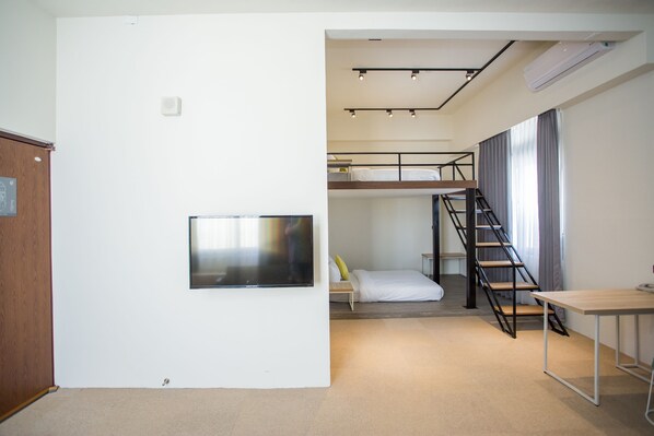 A room with a bunk bed, a desk, and a TV mounted on the wall.