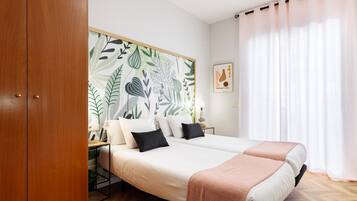 Une chambre avec un grand lit, une armoire en bois, un mur orné d’un motif de feuilles, une table de chevet avec une lampe et une fenêtre avec des rideaux.