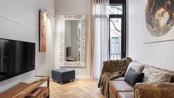 Un salon moderne avec un téléviseur à écran plat, un meuble TV en bois, un pouf gris, un canapé en cuir marron, un plaid à motifs léopard et un grand miroir avec un cadre orné.