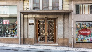 Une façade d’immeuble avec une double porte ornée de motifs métalliques complexes, une enseigne indiquant « Soldes » et une publicité pour « Havaianas » sur la droite.