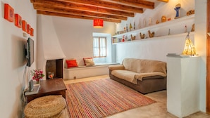 Una sala de estar acogedora con techo de madera, un sofá, un tapete colorido y una estantería con adornos.