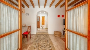 Un pasillo con techo de madera, una zona de comedor con mesa y sillas, un reloj y un tapiz decorativo.