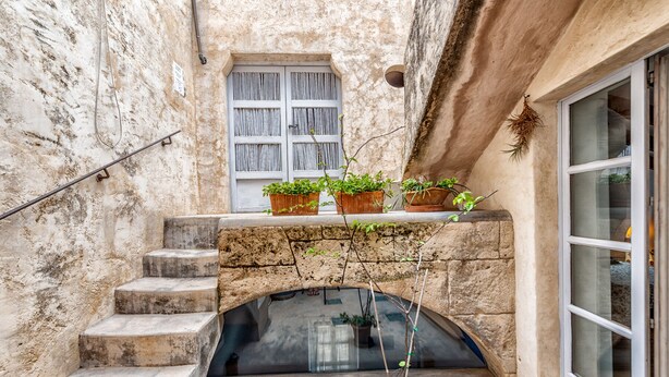Una escalera de piedra conduce a un pequeño patio con una ventana y macetas.