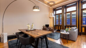 Een moderne woonkamer met een houten eettafel, zwarte stoelen, een grijze bank en een bijzettafeltje met een plant.