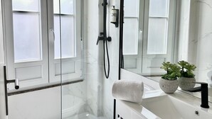 A modern bathroom with a glass-enclosed shower, a white toilet, and a vanity with a mirror and two potted plants. - Well Decorated Studio in Santa Catarina Street (Oporto)