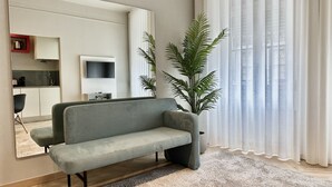 A living room with a grey sofa, a large mirror, a potted plant, and a kitchen area in the background. - Well Decorated Studio in Santa Catarina Street (Oporto)