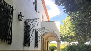 Un edifici amb façana blanca, reixes de ferro negre a les finestres i teulada de teules vermelles.