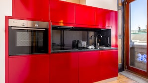 Eine rote Küche mit Einbauofen und Mikrowelle, einer Kaffeemaschine und einem Fenster mit Blick nach draußen.