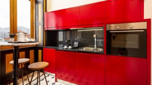 A modern kitchen with red cabinets, a stainless steel oven, and a coffee maker on the countertop. - Authentic Studio in Bolhão Market (Oporto)