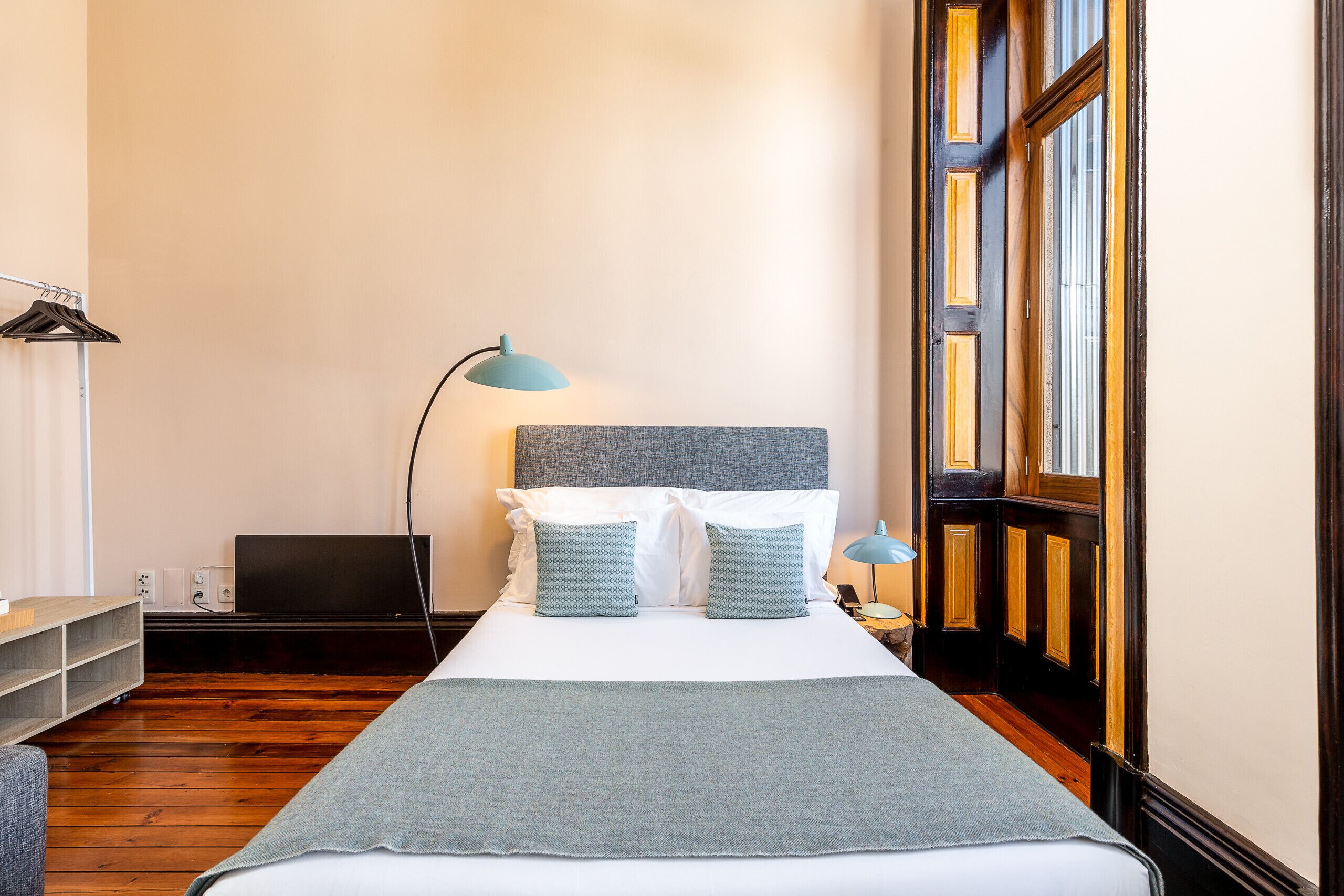 A neatly arranged hotel room with a bed, a desk, a lamp, and a window.