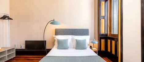 A neatly arranged hotel room with a bed, a desk, a lamp, and a window.