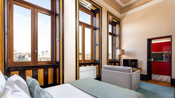 A hotel room with a large bed, a desk with a chair, a TV, and a red door. - Authentic Studio in Bolhão Market (Oporto)