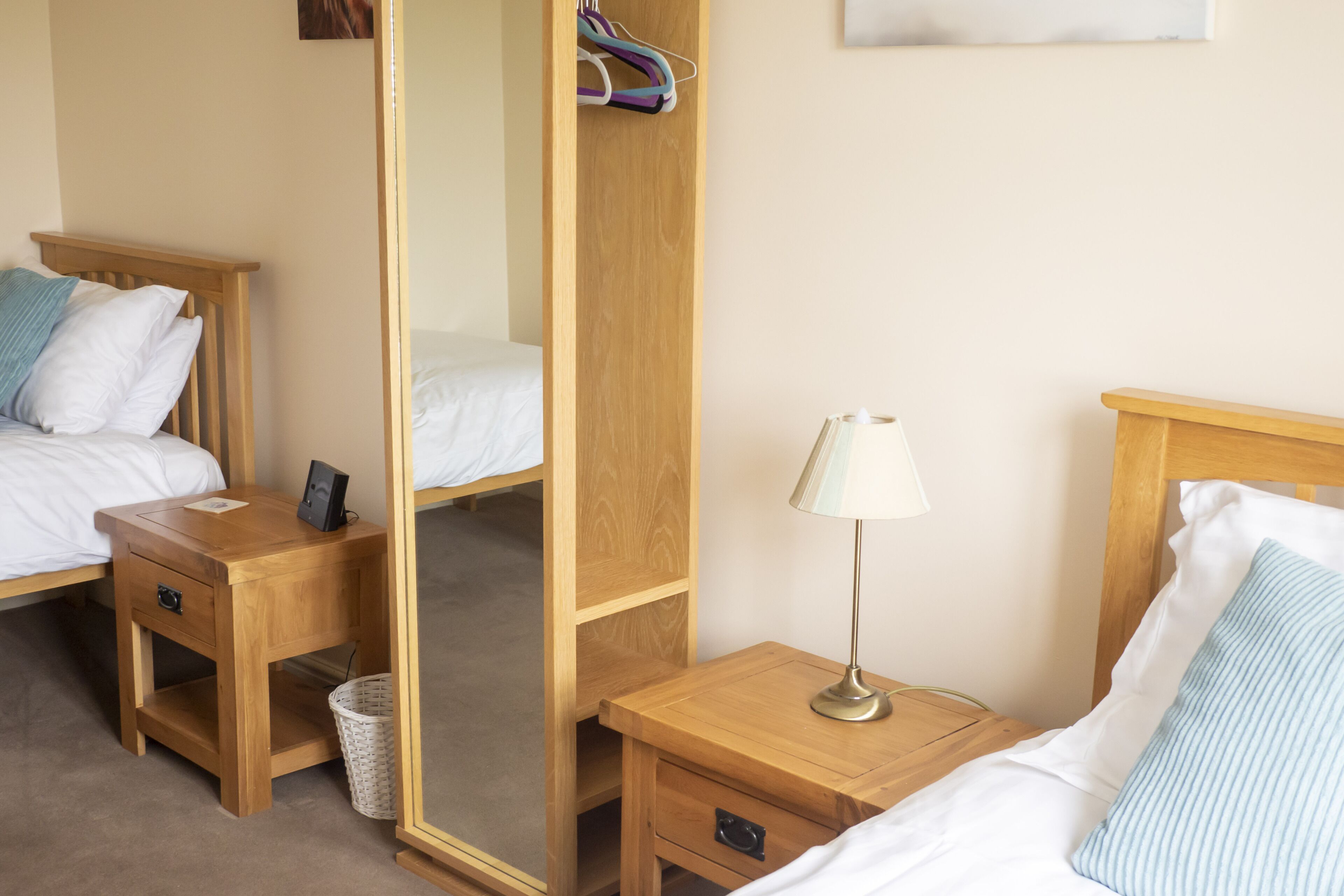 A hotel room with two beds, wooden nightstands, a mirror, and a lamp.