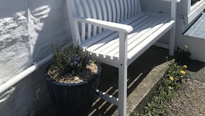 A white bench outside a building with a window and a door.
