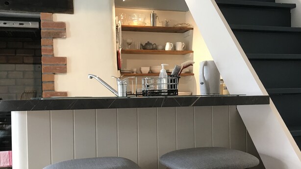 A kitchen with a bar area, including two stools, a sink, and shelves with dishes.