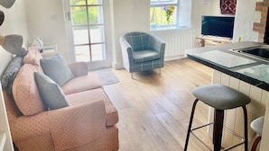 A cozy living room with a sofa, a blue armchair, and a kitchen area with a sink and bar stools.