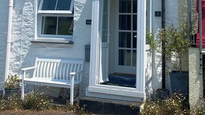 A white two-story house with a chimney, a front door, and a bench outside.