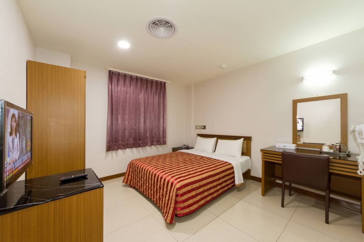 Une chambre d’hôtel équipée d’un lit, d’un bureau, d’une chaise, d’une télévision et d’un miroir.