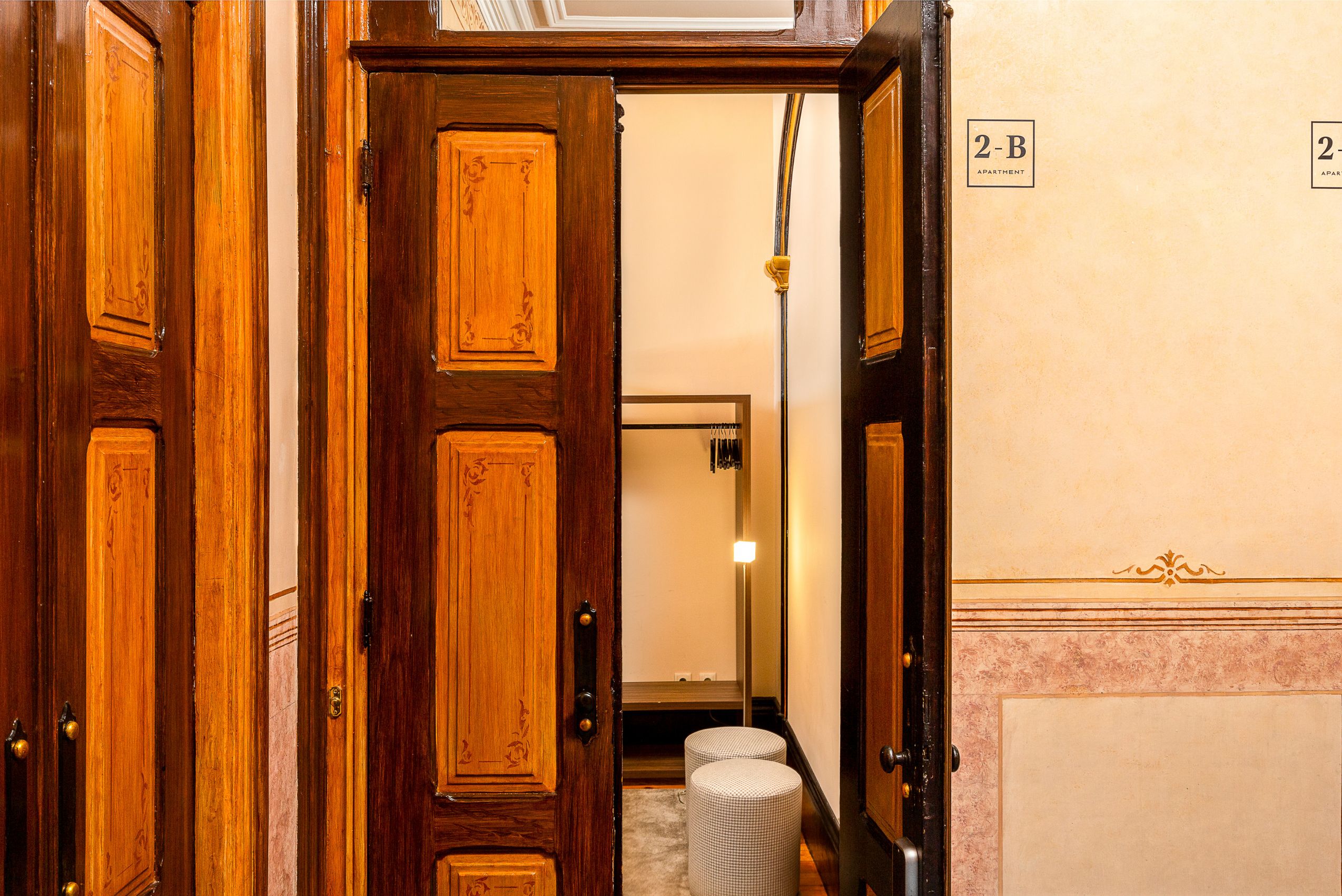 A wooden door leading to a hallway with a mirror and a sign indicating '2-B Apartment'.