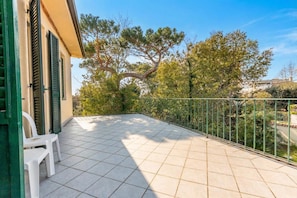 A balcony with a tiled floor, a metal railing, and a white plastic chair.