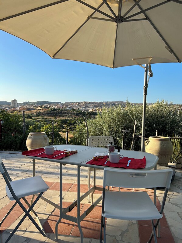 An outdoor patio with a table set for two, a large umbrella, and a view of a cityscape in the background.
