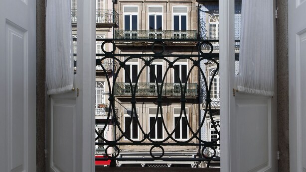 Une porte ouverte, surmontée d’un portail en fer forgé, mène à un bâtiment doté de nombreux balcons et fenêtres.