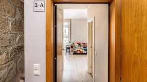 Un couloir mène à une pièce dont l’encadrement de la porte est en bois et sur laquelle est apposée une plaque indiquant « Appartement 2-A ».