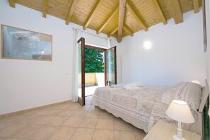 A bedroom with a bed, a nightstand, a lamp, a window with curtains, and a painting on the wall.