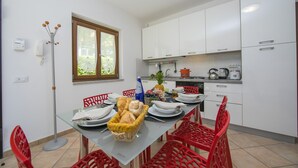 Une cuisine moderne avec des meubles blancs, une table à manger dressée avec des assiettes, du pain et un panier de fruits.