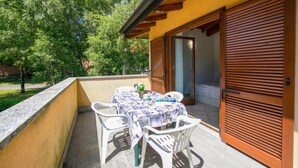 Un balcon avec une table et des chaises, une porte en bois et une vue sur les arbres.