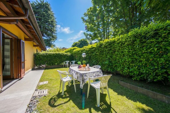 A patio with a table and chairs, surrounded by greenery and a building with a yellow facade.