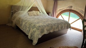 A bedroom with a canopy bed, a rustic stone arch window, and a textured carpet.