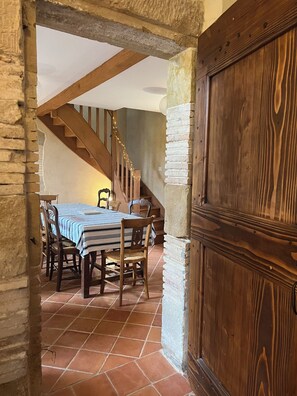 Comedor con una mesa dispuesta para cuatro, sillas de madera, una escalera y una puerta de madera.