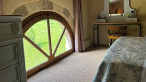 A bedroom with a large arched window, a wooden desk, a mirror, and a bed with a patterned bedspread.