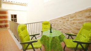 A patio with a round table and four chairs, a bottle of wine, and a view of a building with a white facade and a tiled roof.