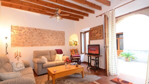 A cozy living room with a wooden ceiling, a stone wall, a television, and a window with curtains.