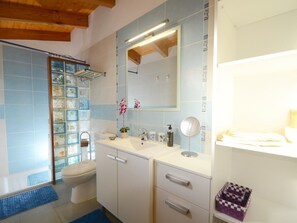 Un bagno con WC, lavandino, specchio e mensole con articoli da toilette.