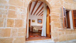 An arched doorway leading into a room with a sofa and a small table, a tiled floor, and a stone wall.