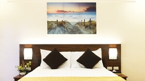 A neatly made bed with a white and yellow bedspread, two dark pillows, and a wooden headboard.